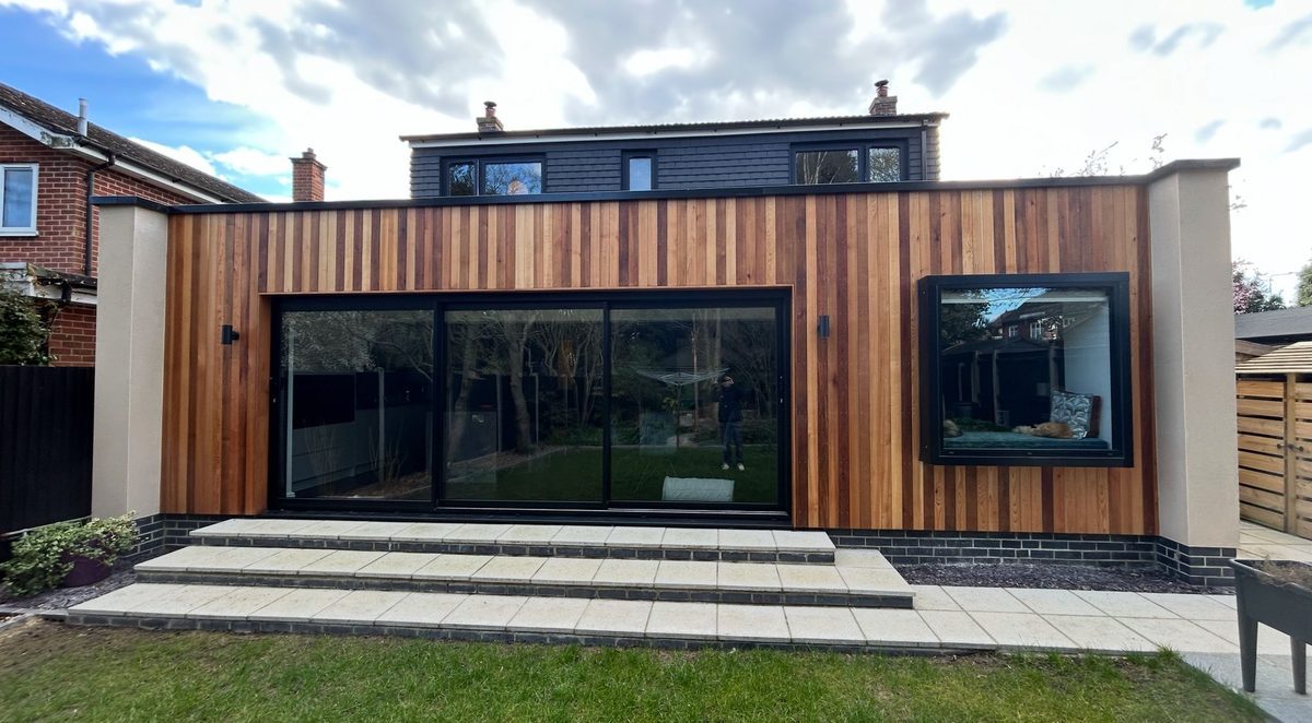 A contemporary cedar clad extension with aluminium sliding doors and a corner picture window, installed by BBH Limited Home Improvements