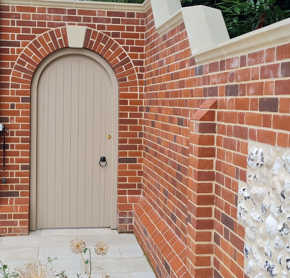 A painted arched pedestrian door made by Countryside Gates and Fencing, fitted to a curved brick opening in a garden wall