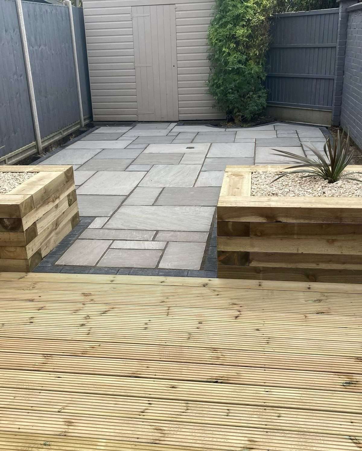 A finished Indian sandstone patio with timber sleeper planters and decking by N.B. O&rsquo;Shea Construction